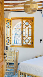 Alhambra Ryad & Spa bedroom featuring white bedding, natural wood furniture, decorative wooden window frames, and blue patterned floor tiles