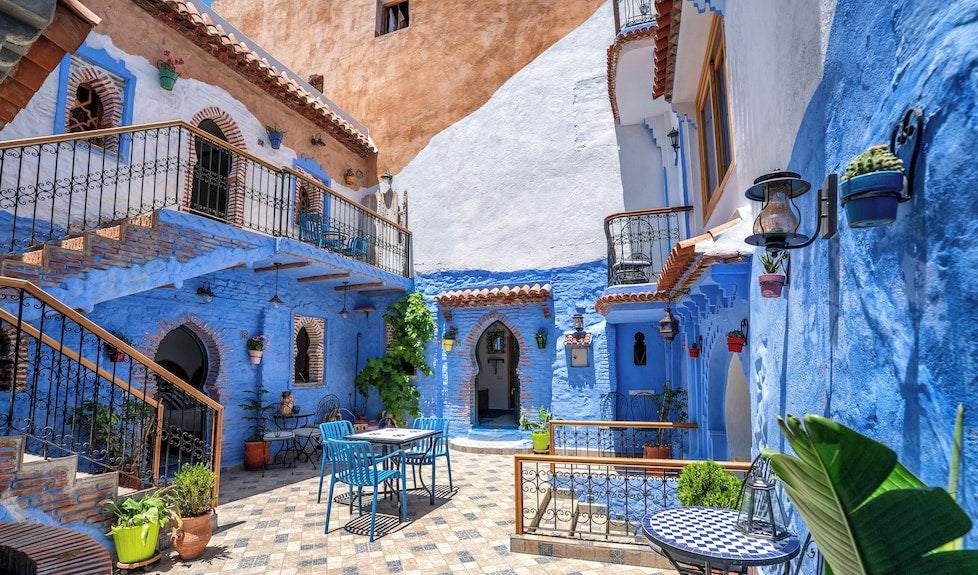 Alhambra Ryad & Spa courtyard with blue-painted walls, traditional Moroccan arches, tiled floors, and outdoor seating