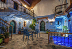 Alhambra Ryad & Spa courtyard with blue painted walls, traditional wooden doors, wrought iron balconies, and tiled floor with metal chairs and tables