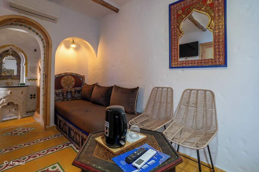 Alhambra Ryad & Spa seating area featuring a brown cushioned bench, woven chairs, ornate mirror, and decorated coffee table