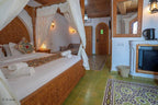 Alhambra Ryad & Spa bedroom with carved wooden canopy bed, white curtains, green tiled floor, and traditional patterns
