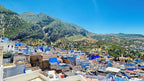 Panoramic view of Chefchaouen with blue and white painted buildings nestled among green mountains under a clear blue sky at Alhambra Ryad & Spa