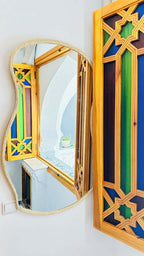Alhambra Ryad & Spa decorative wall mirror with wooden frame featuring intricate green, yellow, and blue geometric patterns reflecting a white arched interior
