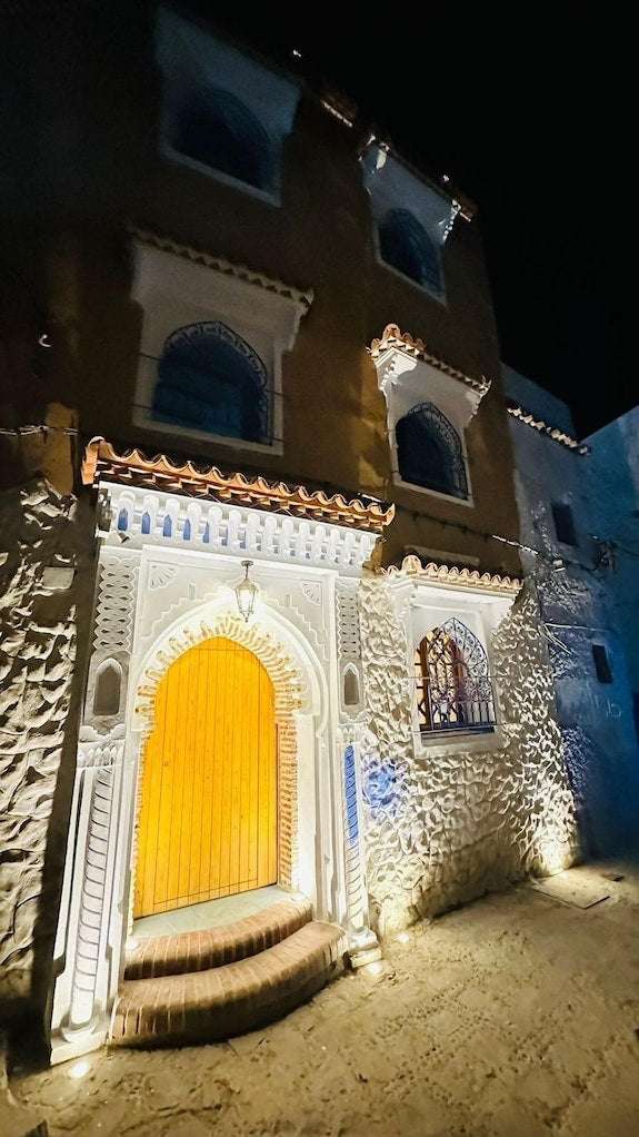 Alhambra Ryad & Spa entrance with illuminated traditional Moroccan wooden door and ornate white stone archway at night