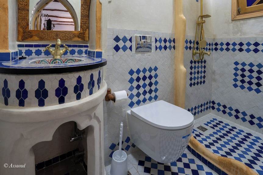 Alhambra Ryad & Spa bathroom with white and blue patterned tiles, a white toilet, and a brass shower fixture