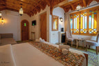 Alhambra Ryad & Spa Moroccan-style bedroom with wooden ceiling, patterned bed runner, stained glass windows, and elegant seating area