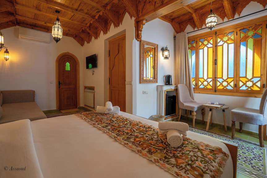 Alhambra Ryad & Spa Moroccan-style bedroom with wooden ceiling, patterned bed runner, stained glass windows, and elegant seating area