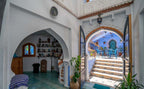 Traditional Moroccan riad interior with white stucco walls, arched doorway, blue tiled floor, and patio stairs leading to a blue courtyard, showcasing Alhambra Ryad & Spa style