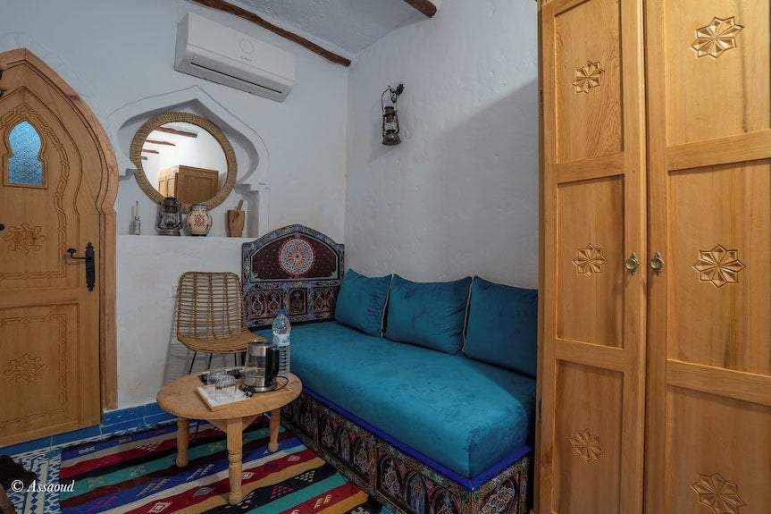 Alhambra Ryad & Spa room with Moroccan-style wooden door, blue cushioned sofa, patterned carpet, and decorative wooden wardrobe