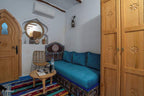 Alhambra Ryad & Spa room with Moroccan-style wooden door, blue cushioned sofa, patterned carpet, and decorative wooden wardrobe