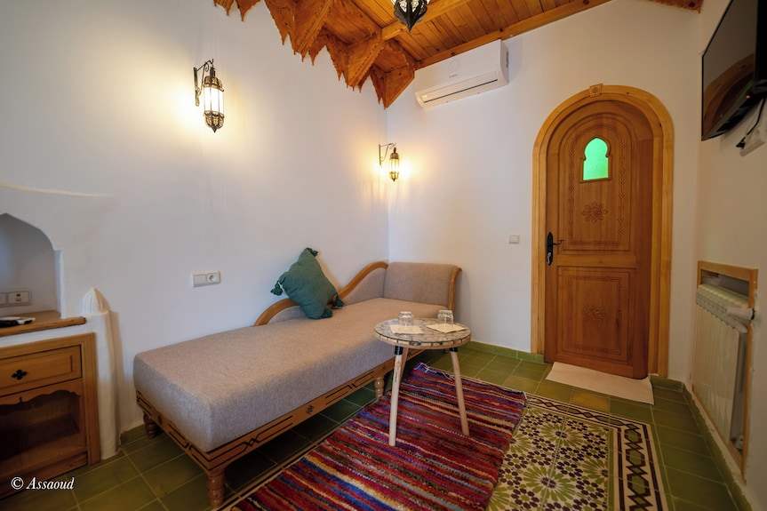 Alhambra Ryad & Spa cozy Moroccan-style room with wooden ceiling, gray sofa, colorful rugs, and arched wooden door