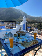 Alhambra Ryad & Spa rooftop breakfast setup with traditional Moroccan tea, orange juice, bread, and scenic mountain views in Chefchaouen