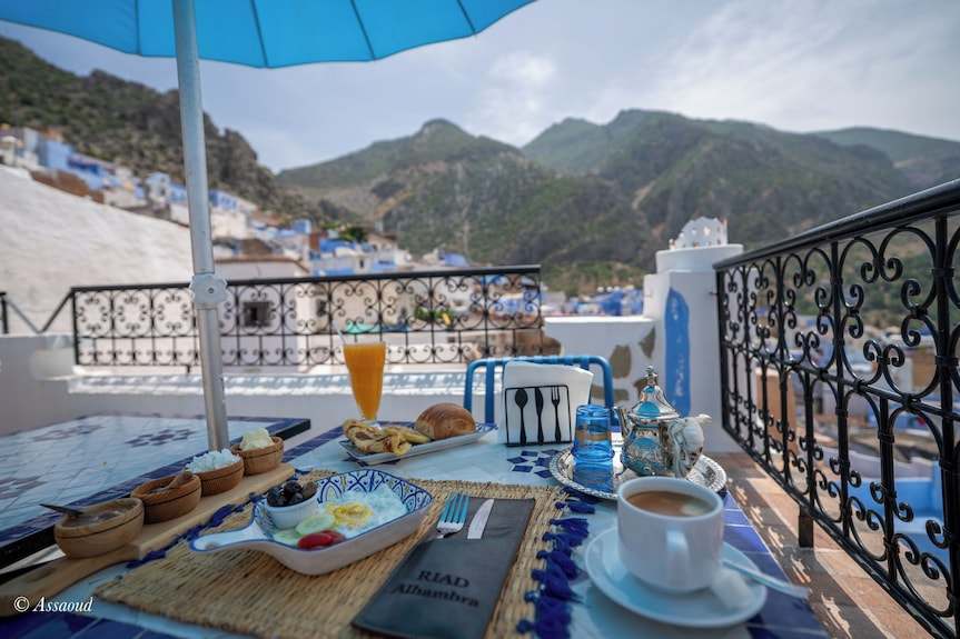 Alhambra Ryad & Spa rooftop terrace breakfast setup with Moroccan tea set, croissants, orange juice, and blue mountain view