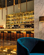 Barcelo Anfa Casablanca hotel bar with warm brass shelving, liquor bottles, marble counter, and blue velvet chair