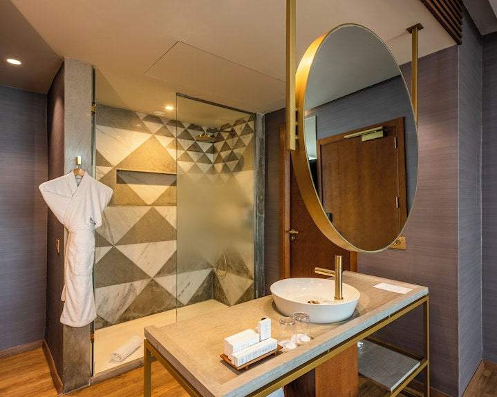 Barcelo Anfa Casablanca hotel bathroom with geometric marble shower, white robe, vessel sink and round mirror