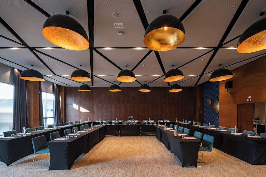 Barcelo Anfa Casablanca hotel conference room with black tables, teal chairs, wood walls, and pendant lighting