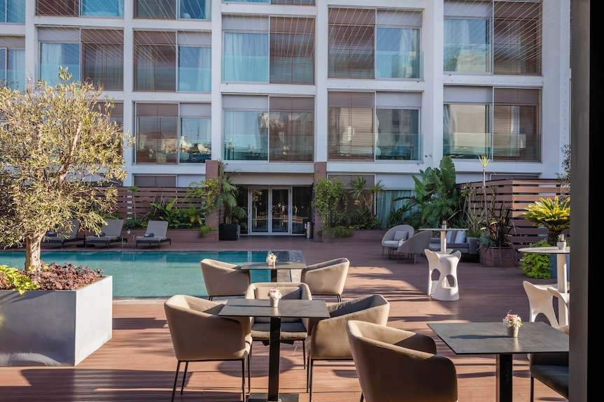 Barcelo Anfa Casablanca hotel courtyard with turquoise pool, outdoor dining tables, plants, and modern glass facade