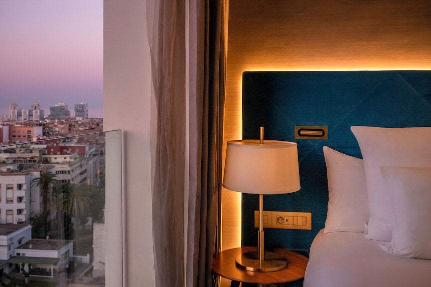 Barcelo Anfa Casablanca hotel room with blue upholstered headboard, white bedding, bedside lamp, and city view