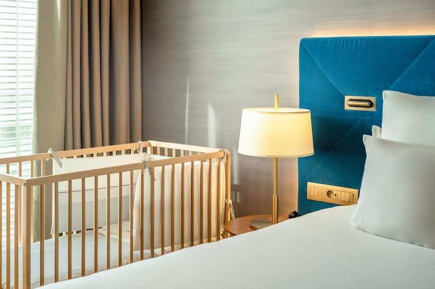 Barcelo Anfa Casablanca hotel room with white bed, blue upholstered headboard, lamp, and wooden baby crib