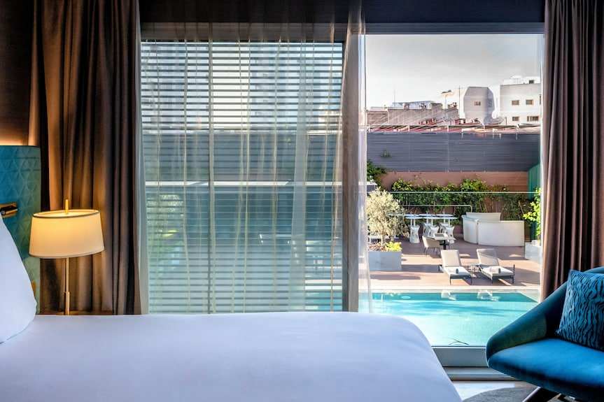 Barcelo Anfa Casablanca hotel room with white bedding, dark curtains, blue chair, and pool terrace view