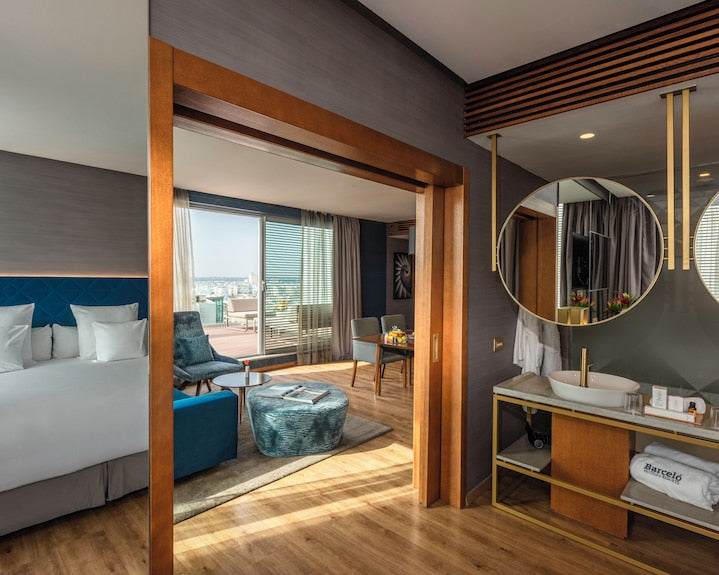 Barcelo Anfa Casablanca hotel suite with white bed, blue seating, wood accents, and round mirrored bathroom vanity