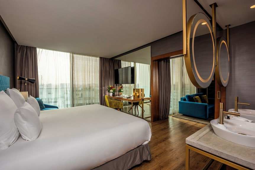 Barcelo Anfa Casablanca hotel room with white bed, teal seating, wood furnishings, mirrored wall and freestanding bathtub