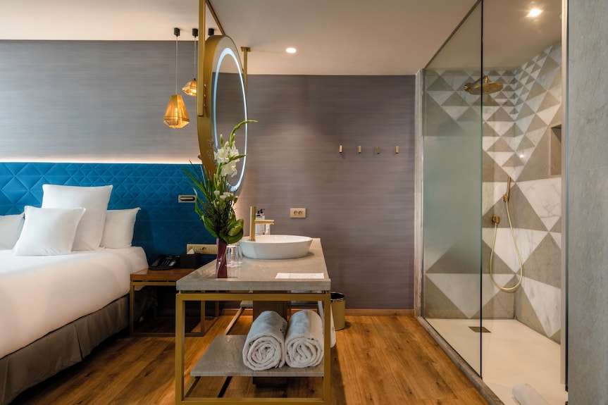 Barcelo Anfa Casablanca hotel room with white bed, blue geometric headboard, vanity, towels, and glass shower