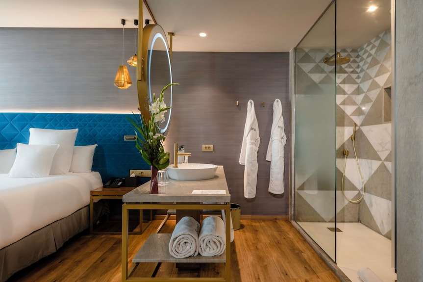Barcelo Anfa Casablanca hotel room with white bedding, blue quilted headboard, marble vanity, robes, and glass shower