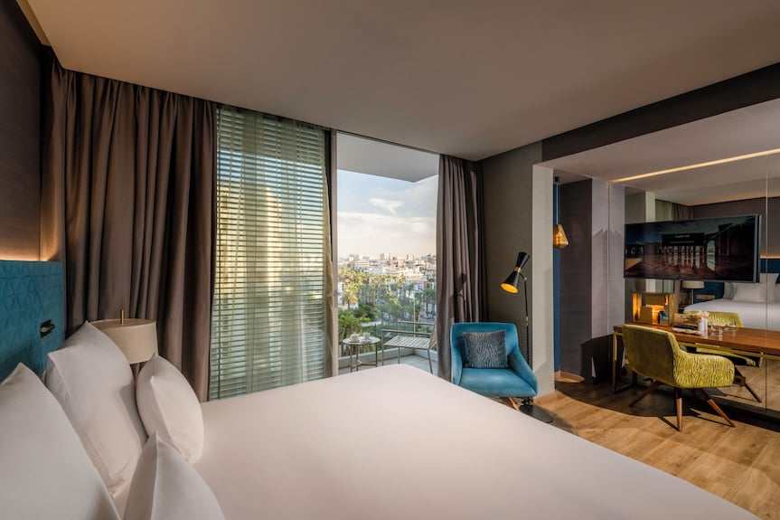 Barcelo Anfa Casablanca hotel room with white bed, teal headboard, blue armchair, and city-view balcony
