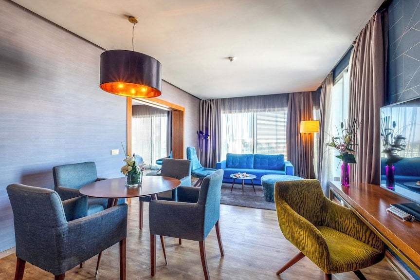 Barcelo Anfa Casablanca hotel suite with modern blue and grey seating, patterned yellow chair, dining table, and large windows