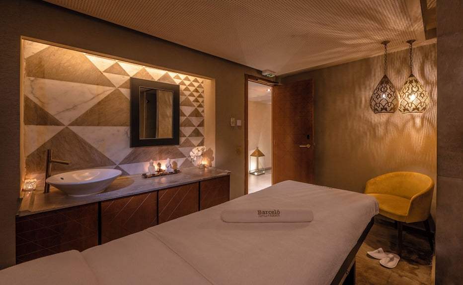 Barcelo Anfa Casablanca spa treatment room with beige massage table, marble geometric wall, sink, pendant lamps and yellow chair