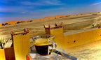 Berber Palace Hotel view featuring a clear blue sky, sandy landscape, and traditional yellow desert walls with a glass cup of black coffee in the foreground