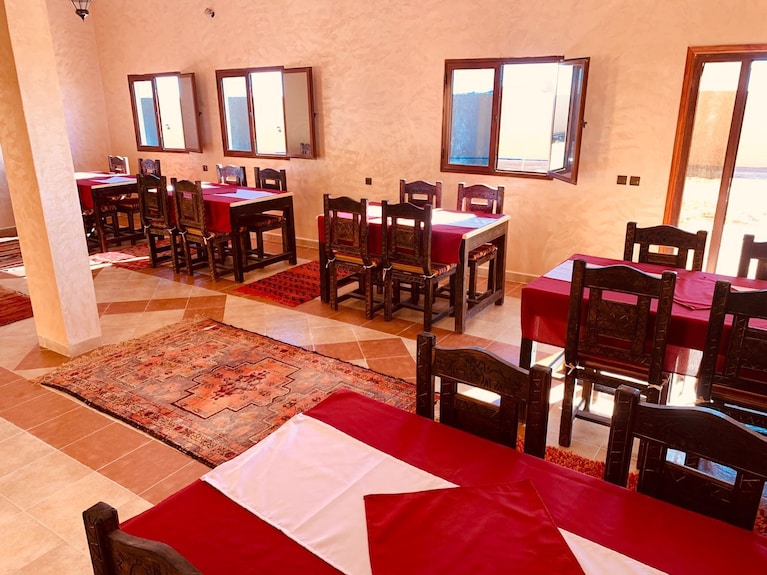 dining area at Berber Palace Hotel featuring wooden chairs, tables with red and white linens, and beige tiled floors