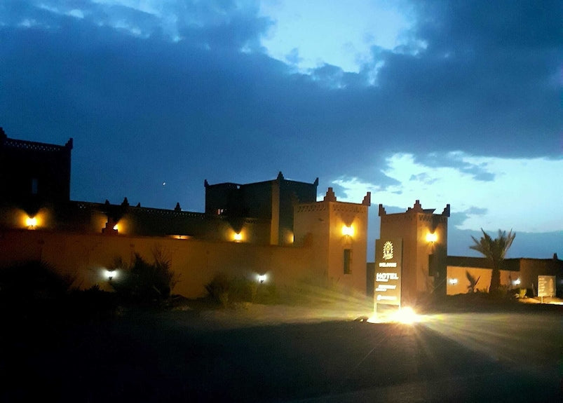 Berber Palace Hotel exterior at dusk with illuminated traditional Moroccan architecture and entrance sign glowing warmly