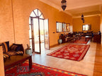 Berber Palace Hotel indoor seating area with terracotta walls, wooden furniture, patterned cushions, and red geometric rugs