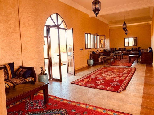 Berber Palace Hotel indoor seating area with terracotta walls, wooden furniture, patterned cushions, and red geometric rugs