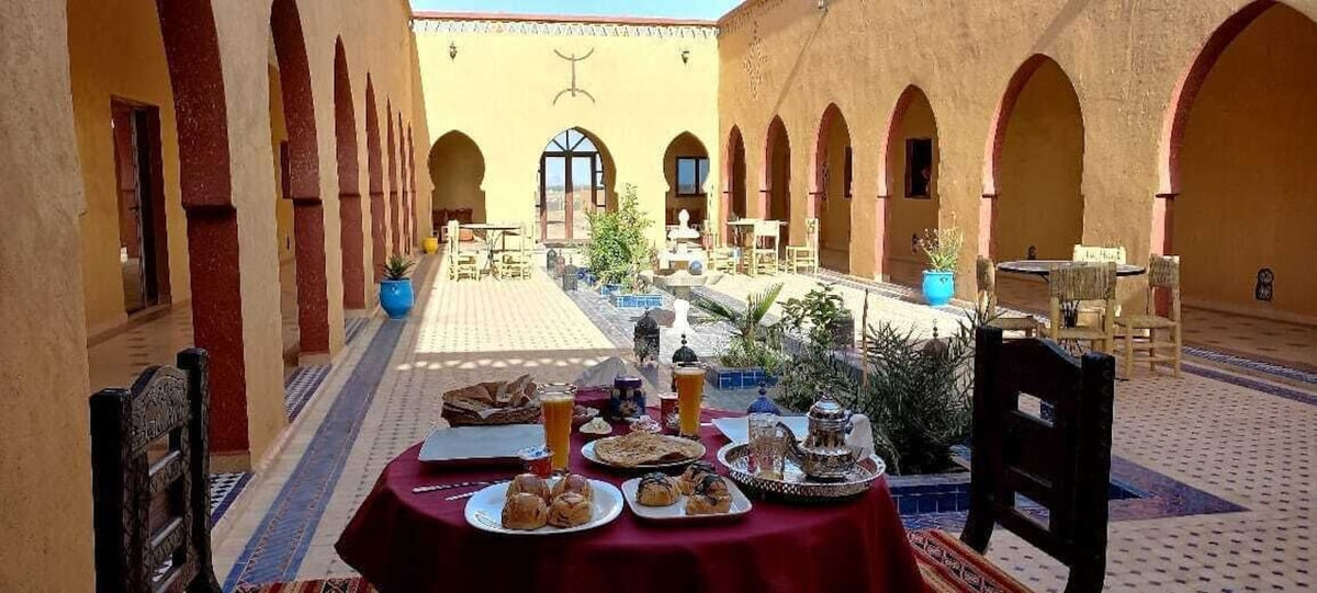 Berber Palace Hotel courtyard with terracotta walls, arched doorways, tiled floor, and a red table set with Moroccan breakfast dishes and tea service