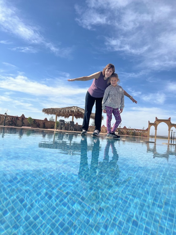 Berber Palace Hotel large outdoor blue-tiled pool with clear water and sky reflections, with two people posing by the edge