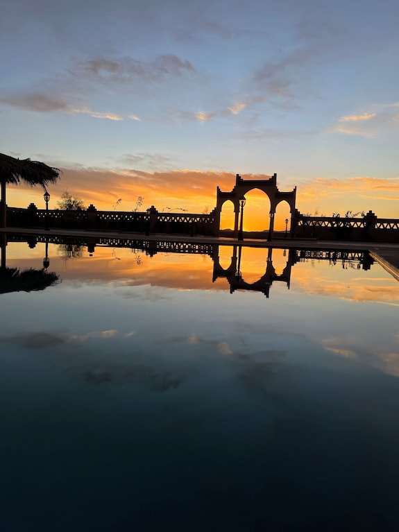 Berber Palace Hotel outdoor pool at sunset with ornate archway reflection and vibrant orange sky