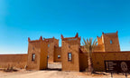 Berber Palace Hotel with traditional Moroccan adobe architecture in sandy brown color under clear blue sky