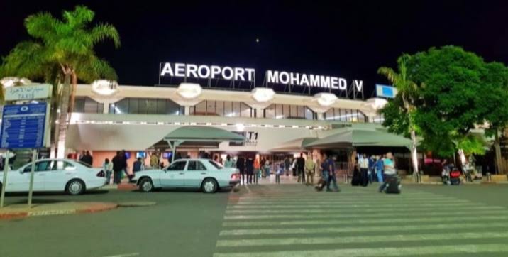 airport terminal building at night with illuminated sign reading AEROPORT MOHAMMED V and people with luggage