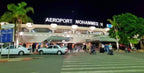 airport terminal building at night with illuminated sign reading AEROPORT MOHAMMED V and people with luggage
