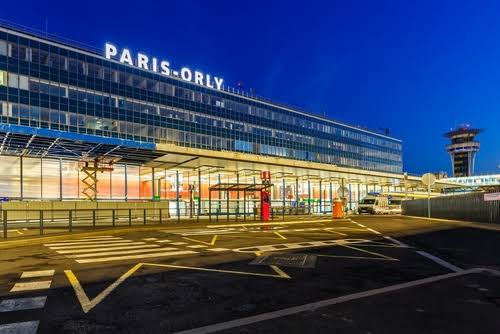Airport terminal at Paris Orly with illuminated exterior glass facade and control tower at dusk, ideal for Book flight tickets