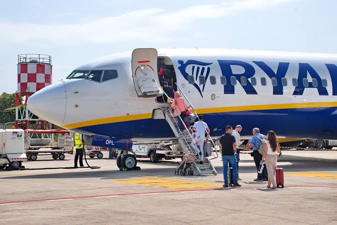 Book flight tickets showing passengers boarding a white Ryanair airplane with blue and yellow accents on the runway