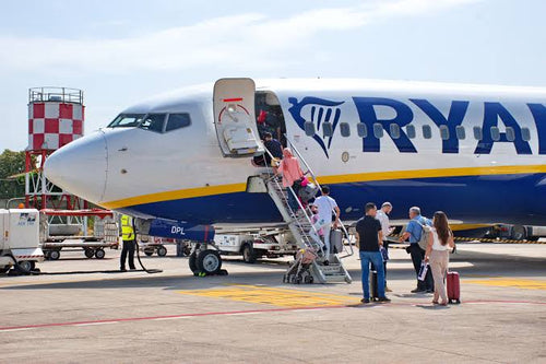 Book flight tickets showing passengers boarding a white Ryanair airplane with blue and yellow accents on the runway
