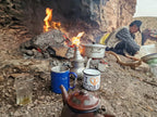 Outdoor Moroccan tea setup with metal teapot, blue and white mugs near open fire and man preparing tea on Boumalne Dades Tour