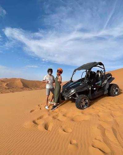 Off-road black and green buggy with two people wearing helmets standing beside it on golden sand dunes during a Buggy Rental in Merzouga adventure