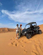 Off-road black and green buggy with two people wearing helmets standing beside it on golden sand dunes during a Buggy Rental in Merzouga adventure