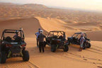 Off-road black and gray buggies parked on golden sand dunes with people wearing helmets for Buggy Rental in Merzouga adventure.