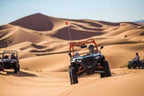 Off-road orange and black dune buggy with drivers riding across golden sand dunes during Buggy Rental in Merzouga desert adventure